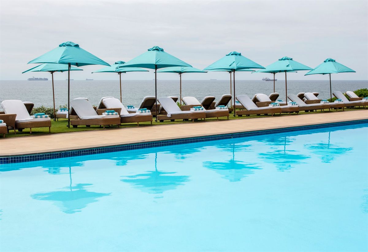 Turquoise umbrellas and sun loungers beside a pool overlooking the sea
