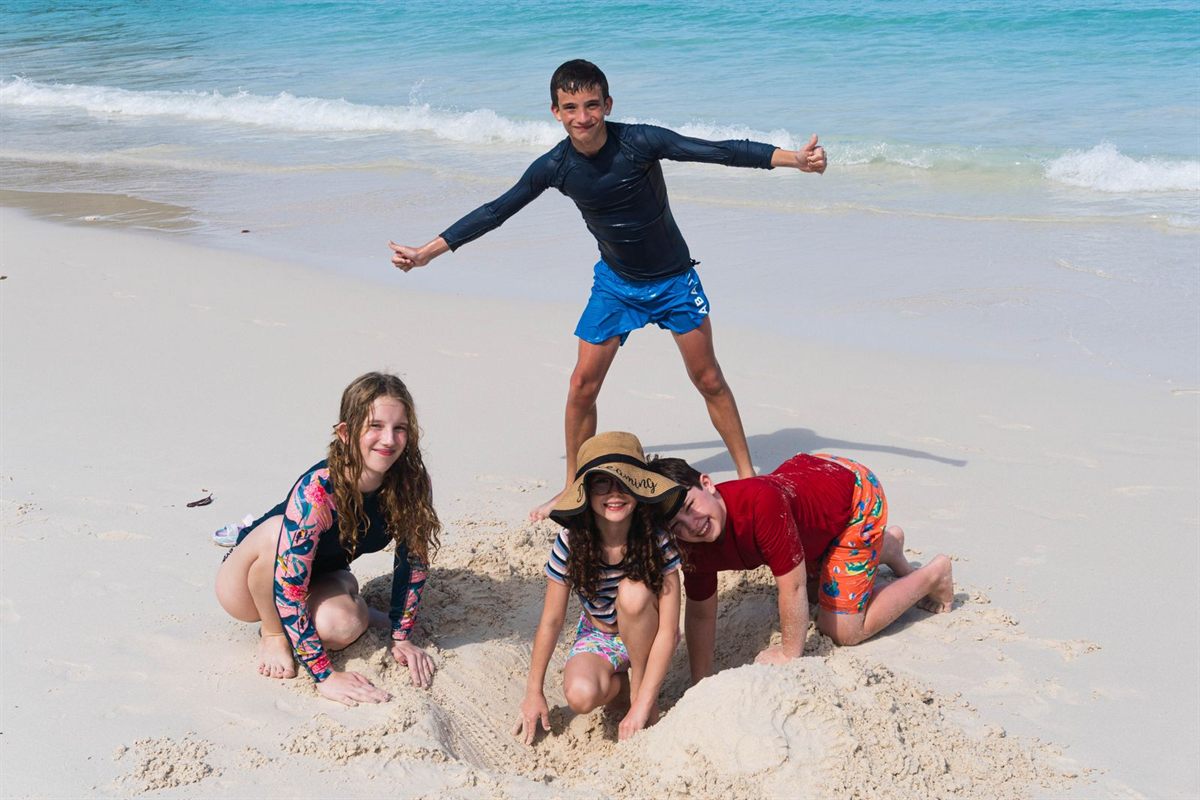 A family of four playing together on a white sand beach
