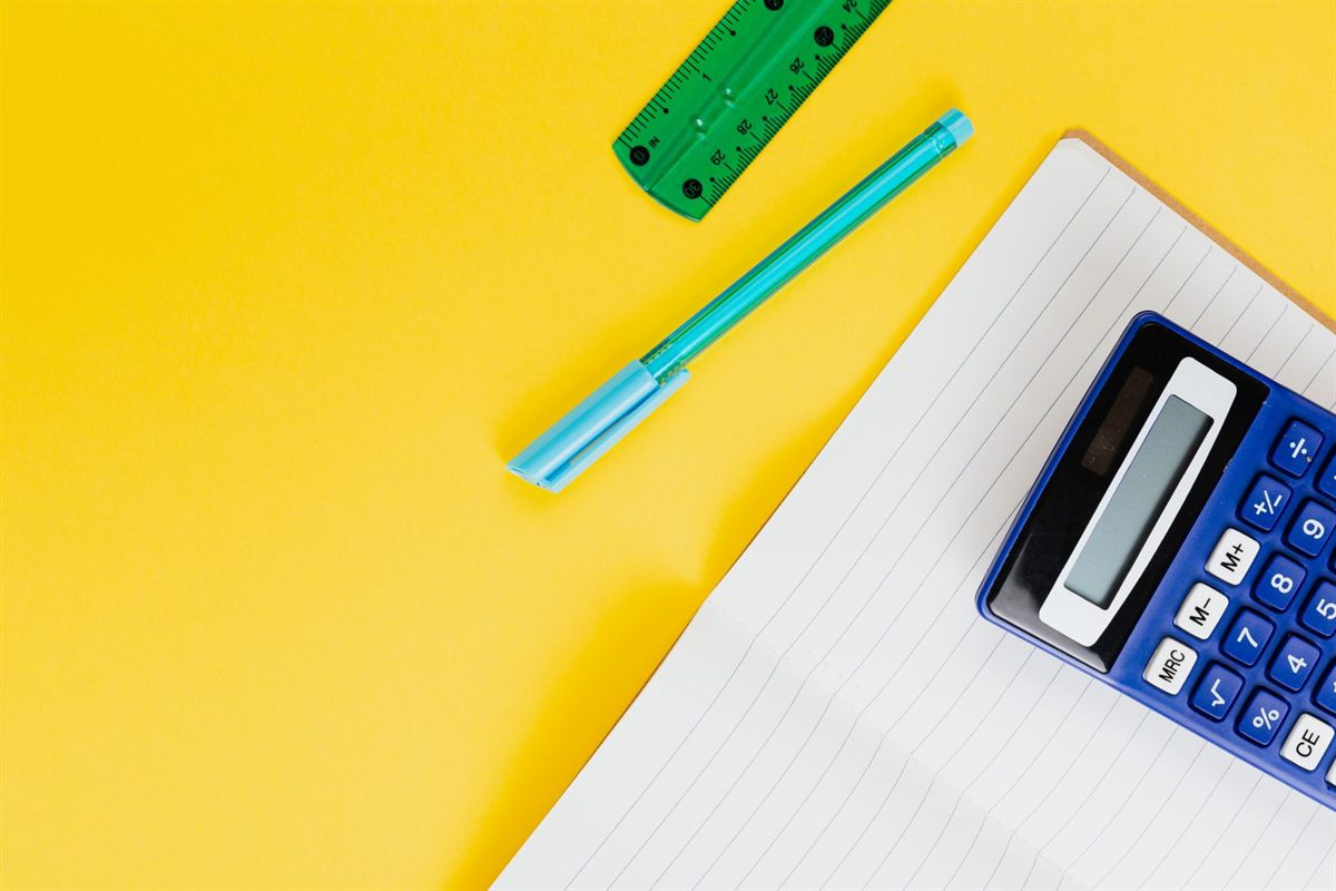 A calculator, notebook and pens on a bright yellow desk for planning a trip