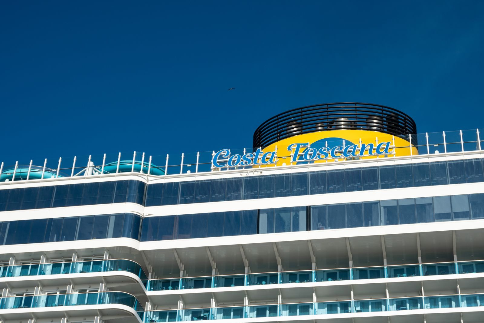 The funnel and upper decks of a large cruise ship against a deep blue sky