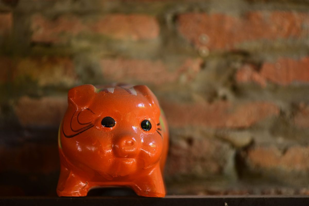 An orange piggy bank on a shelf against a brick wall
